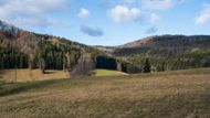 Za lesem jsou dlouhé lány a pole, z nichž je výhled na hřebeny Ještědsko-kozákovského hřbetu.