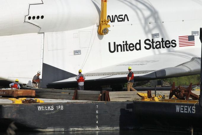 Workers secure the Space Shuttle Enterprise while it is being lifted onto a barge at John F. Kennedy International Airport's harbor for a four-day journey to the Intrepid Sea, Air & Space Museum in New York June 2, 2012. REUTERS/Eduardo Munoz (UNITED STATES - Tags: TRANSPORT SCIENCE TECHNOLOGY) Published: Čer. 2, 2012, 10:27 odp.