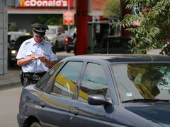 Policista uděluje pokutu řidiči zeleného Escortu za parkování v těsné blízkosti křižovatky a přechodu pro chodce.