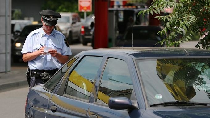 Policista uděluje pokutu řidiči zeleného Escortu za parkování v těsné blízkosti křižovatky a přechodu pro chodce.