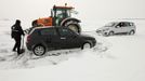 A tractor tows a car as a man shovels snow off his car on a snow-covered road at Epinoy near Cambrai, northern France, March 12, 2013 as winter weather with snow and freezing temperatures returns to northern France. REUTERS/Pascal Rossignol (FRANCE - Tags: TRANSPORT ENVIRONMENT) Published: Bře. 12, 2013, 4:30 odp.