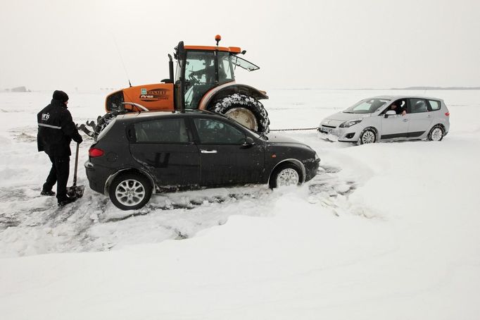 A tractor tows a car as a man shovels snow off his car on a snow-covered road at Epinoy near Cambrai, northern France, March 12, 2013 as winter weather with snow and freezing temperatures returns to northern France. REUTERS/Pascal Rossignol (FRANCE - Tags: TRANSPORT ENVIRONMENT) Published: Bře. 12, 2013, 4:30 odp.