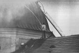 Muž s požární hadicí se snaží uhasit požár střechy ohrožující jednu z věží areálu Svatá Hora.