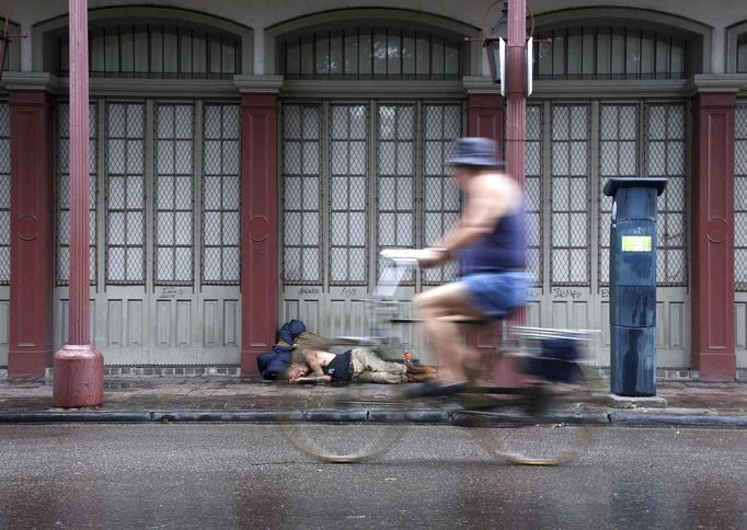 A New Orleans resident cycles past a homeless man sleeping on a sidewalk in the French Quarter as Hurricane Isaac approaches New Orleans, Louisiana August 28, 2012. REUTERS/Jonathan Bachman (UNITED STATES - Tags: ENVIRONMENT DISASTER) Published: Srp. 28, 2012, 8:53 odp.