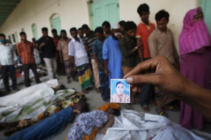 A relative holds a picture of a garment worker who is missing, in front of the remains of people who died inside the rubble of the collapsed Rana Plaza building, in Savar, 30 km (19 miles) outside Dhaka April 25, 2013. The number of people killed by the collapse of a building in Bangladesh's capital rose to 147 overnight and the death toll could climb further because many people are still trapped inside, Dhaka's district police chief told Reuters on Thursday. REUTERS/Andrew Biraj (BANGLADESH - Tags: DISASTER) Published: Dub. 25, 2013, 3:31 dop.