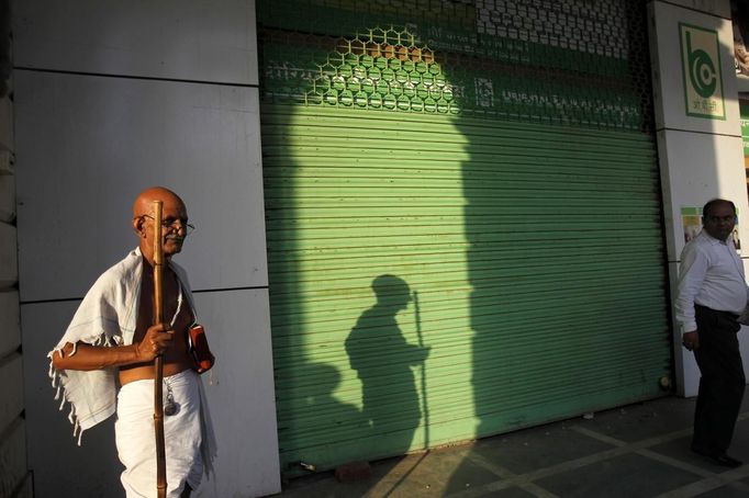 Mahesh Chaturvedi (L), 63, who dresses up like Mahatma Gandhi, stands outside a closed shop in New Delhi September 28, 2012. Chaturvedi says that the soul of Gandhi resides in him and he has been sent to continue the work of Father of the Nation. After his self proclaimed transformation in 2002 as Gandhi, Chaturvedi has been travelling extensively and plays up to his startling resemblance to Gandhi at protests and demonstrations. Picture taken September 28, 2012. REUTERS/Mansi Thapliyal (INDIA - Tags: SOCIETY) Published: Lis. 26, 2012, 3:54 dop.