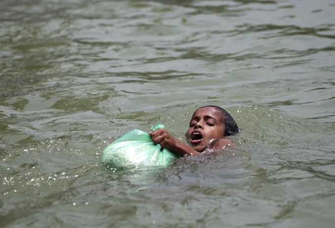 A boy, who is affected by flood swims with a bag of food distributed by local organizations in Sylhet June 30, 2012. At least 100 people have died and 250,000 left stranded by flash floods and landslides in Bangladesh set off by the heaviest rain in years. The low-lying and densely populated country, which is in its wet season, has been battered by five days of torrential downpours. REUTERS/Andrew Biraj (BANGLADESH - Tags: SOCIETY DISASTER ENVIRONMENT) Published: Čer. 30, 2012, 4:08 odp.