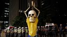 Military policemen stand in a line behind a demonstrator wearing the figure of a skeleton holding up a trophy representing that of the FIFA World Cup during a protest aga