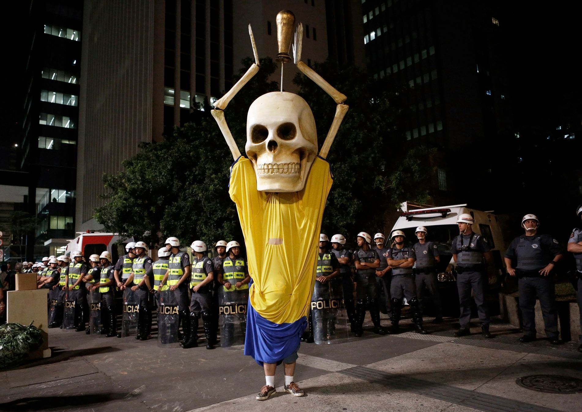 Military policemen stand in a line behind a demonstrator wearing the figure of a skeleton holding up a trophy representing that of the FIFA World Cup during a protest against the 2014 World Cup, in Sa
