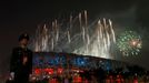 Policista stojí na stráži. Za ním září ohňostroj olympijského ceremoniálu nad Národním stadionem v Pekingu.