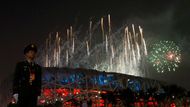 Policista stojí na stráži. Za ním září ohňostroj olympijského ceremoniálu nad Národním stadionem v Pekingu.