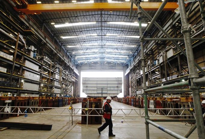 A worker passes the forward section of the aircraft carrier HMS Queen Elizabeth as it is moved onto a barge at HM Naval Base in Portsmouth, southern England May 14, 2012. The hull will be transported by a sea going barge to Rosyth in Scotland where the ship will be assembled in dry dock. REUTERS/Luke MacGregor (BRITAIN - Tags: BUSINESS EMPLOYMENT MILITARY) Published: Kvě. 14, 2012, 2:57 odp.