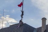 Převlečeni za kominíky umělci vylezli po lešení na střechu Pražského hradu a standartu vyměnili za obří rudé trenýrky. Vlajku zavinuli do balíčku a hodili k nedaleké kavárně Starbucks.