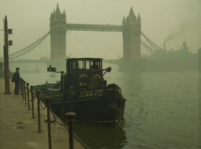 Remorkér na řece Temži poblíž Tower Bridge, Londýn, 1952. Ikonický most je sotva viditelný v hustém smogu, který byl vyvrcholením staletí znečištění. Kolorováno