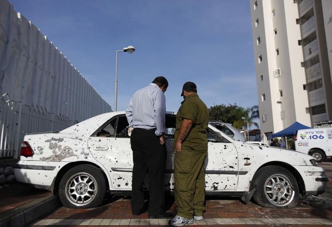 An Israeli soldier (R) and a civilian survey the damage to a car after a rocket fired from Gaza landed in the southern city of Ashdod November 16, 2012. Israel has started drafting 16,000 reserve troops, the military said on Friday, in a sign that violence could escalate further with Palestinian militants in the Gaza Strip. REUTERS/Amir Cohen (ISRAEL - Tags: POLITICS CIVIL UNREST MILITARY) Published: Lis. 16, 2012, 7:39 dop.