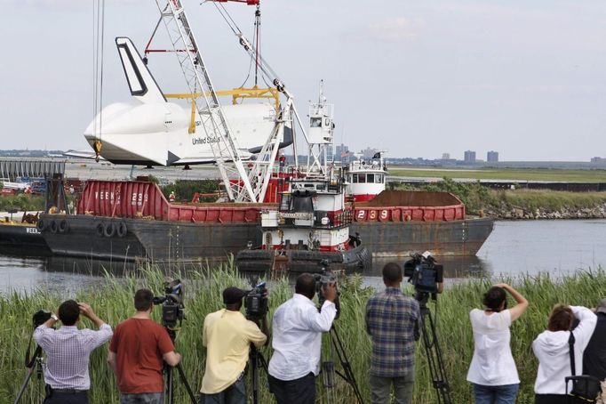 Media members report on the Space Shuttle Enterprise being craned onto a barge at John F. Kennedy International Airport's harbor, for a four-day journey to the Intrepid Sea, Air & Space Museum in New York June 2, 2012.. REUTERS/Michael Berrigan (UNITED STATES - Tags: TRANSPORT SCIENCE TECHNOLOGY) Published: Čer. 2, 2012, 9:49 odp.