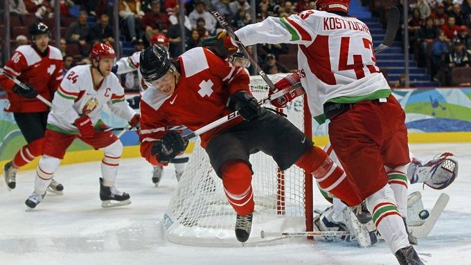 Kostjučenok z Běloruska sráží Švýcara Dicka během osmifinále hokejového turnaje.