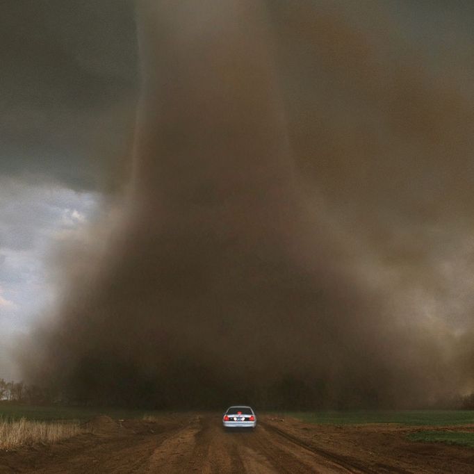 A Very Close Call Original caption:A tornado with large Liberty Bell-shaped debris cloud swirls across a dirt road less than 500 feet in front of a car. Digitally compositied.