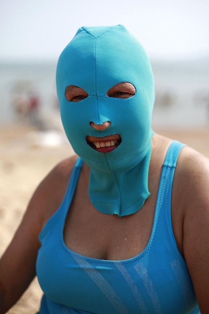 A woman, wearing a nylon mask, smiles as she rests on the shore during her visit to a beach in Qingdao, Shandong province July 6, 2012. The mask, which was invented by a woman about seven years ago, is used to block the sun's rays. The mask is under mass production and is on sale at local swimwear stores. REUTERS/Aly Song (CHINA - Tags: SOCIETY TRAVEL ENVIRONMENT) Published: Čec. 6, 2012, 4:26 odp.