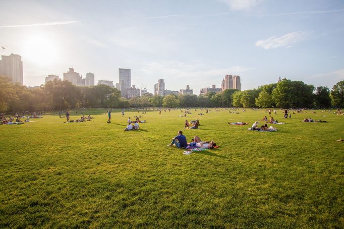 Návštěvníci Central Parku odpočívají za slunečného dne na louce v Manhattanu v New Yorku.