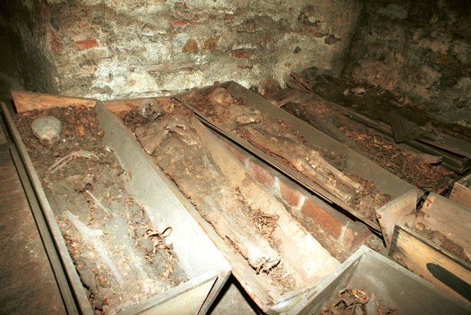 Mumie v rakvích v kryptě kostela Panny Marie Vítězné na Malé Straně. Snímek z roku 1995 ukazuje stav ostatků před asanací a záchranou.