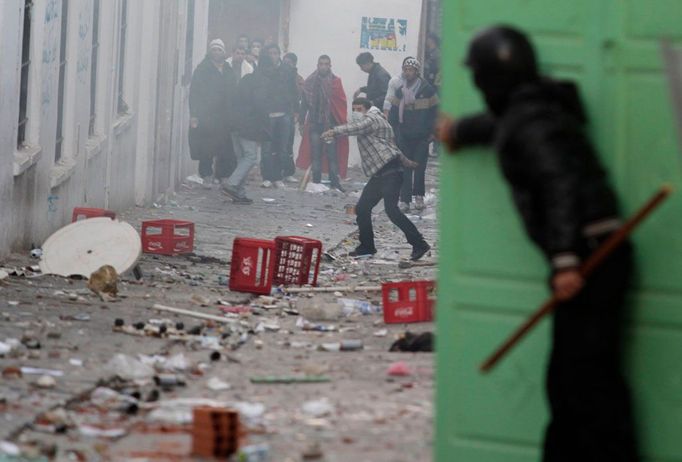 Policista v Tunisu se kryje dveřmi, demonstranti házejí kamením. Snímek byl pořízen 28. ledna 2011.