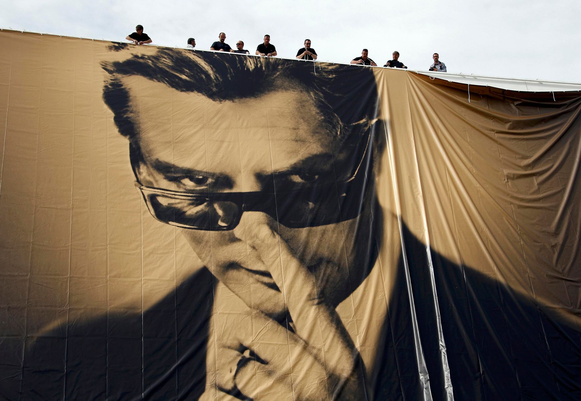 Workers set up a giant canvas of the official poster of the 67th Cannes Film Festival featuring actor Marcello Mastroianni on the Festival Palace in Cannes