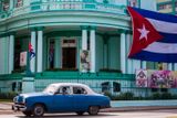Kuba. Auto projíždí kolem budovy s vlajkou spuštěnou na půl žerdi v Havaně.