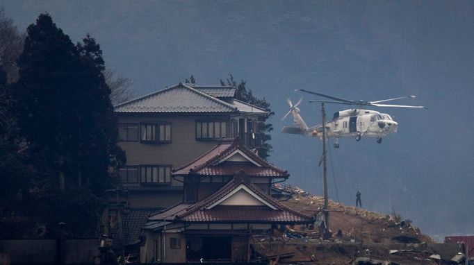 Záchranná helikoptéra spouští jednoho z mužů mezi trosky předměstí Kesennumy.