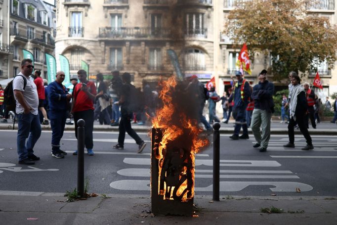 Demonstranti kráčí kolem hořícího odpadkového koše během demonstrace v Paříži v rámci celonárodní stávky a protestů proti vládě.
