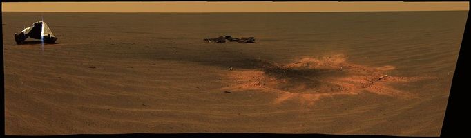 Impressive Impact This stunning image features the heat shield impact site of NASA's Mars Exploration Rover Opportunity. This is an approximately true-color mosaic of panoramic camera images taken through the camera's 750-, 530-, and 430-nanometer filters. The mosaic was acquired on Opportunity's sol 330 (Dec. 28, 2004), shortly after Opportunity arrived to investigate the site where its heat shield hit the ground south of "Endurance Crater" on Jan. 24, 2004. On the left, the main heat shield piece is inverted and reveals its metallic insulation layer, glinting in the sunlight. The main piece stands about 1 meter tall (about 3.3 feet) and about 13 meters (about 43 feet) from the rover. The other large, flat piece of debris near the center of the image is about 14 meters (about 46 feet) away. The circular feature on the right side of the image is the crater made by the heat shield's impact. It is about 2.8 meters (9.2 feet) in diameter but only about 5 to 10 centimeters (about 2 to 4 inches) deep. The crater is about 6 meters (about 20 feet) from Opportunity in this view. Smaller fragments and debris can be seen all around the impact site. The impact excavated a large amount of reddish subsurface material. Darker materials cover part of the crater's flat floor and have formed a streak or jet of material pointing toward the two largest heat shield fragments. Image credit: NASA/JPL/Cornell