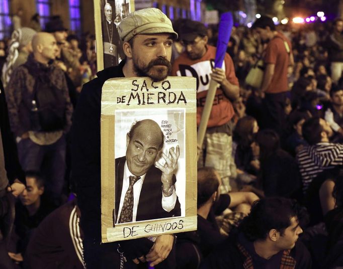 A protester leans on his sign showing Spain's Economy Minister Luis de Guindos and reading "Sack of Shit" as anti-austerity demonstrators continued into the night near the Spanish parliament in Madrid September 25, 2012. Anti-austerity demonstrators protested in Madrid ahead of the government's tough 2013 budget that will cut into social services as the country teeters on the brink of a bailout. REUTERS/Paul Hanna (SPAIN - Tags: POLITICS CIVIL UNREST BUSINESS) TEMPLATE OUT Published: Zář. 25, 2012, 10:58 odp.