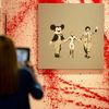 A woman photographs work by artist Banksy at Banksy: The Unauthorised Retrospective exhibition at Sotheby's S2 Gallery in London