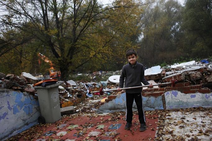 David Valdes Armendia, 7, lifts weights he found amidst debris as a bulldozer (L) demolishes the former school, where his grandparents lived at, in the Spanish gypsy settlement of Puerta de Hierro, in the outskirts of Madrid November 20, 2012. Fifty-four families have been living in Puerta de Hierro, on the banks of the Manzanares river for over 50 years. Since the summer of 2010, the community has been subject to evictions on the grounds that the dwellings are illegal. Families, whose homes have been demolished, move in with relatives whose houses still remain while the debris keeps piling up around them as more demolitions take place. REUTERS/Susana Vera (SPAIN - Tags: CIVIL UNREST BUSINESS CONSTRUCTION) Published: Lis. 20, 2012, 4:54 odp.