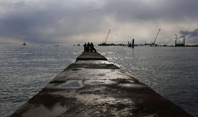 Men fish from a pier at the seafront of Sochi, the host city for the Sochi 2014 Winter Olympics February 18, 2013. Although many complexes and venues in the Black Sea resort of Sochi mostly resemble building sites that are still under construction, there is nothing to suggest any concern over readiness. Construction will be completed by August 2013 according to organizers. The Sochi 2014 Winter Olympics opens on February 7, 2014. REUTERS/Kai Pfaffenbach (RUSSIA - Tags: CITYSCAPE BUSINESS CONSTRUCTION ENVIRONMENT SPORT OLYMPICS) Published: Úno. 18, 2013, 6:46 odp.