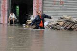 Muž se brodí zaplavenou ulicí města Čchung-čching a přidržuje se lana, aby ho nesmetl proud vody. V sousední provincii Kuang-tung voda zaplavila domy až po střechu.