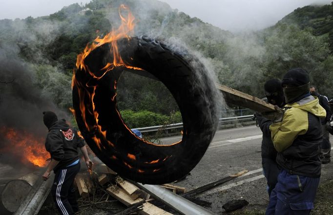 A coal miner uses a plank to carry a burning tire to be used as a barricade in front of the main gate of the "Pozo Santiago" mine in Caborana, near Oviedo, northern Spain June 18, 2012. Spanish coal mining unions are taking part in a general strike in northern Spain mining areas to protest against government action to cut coal subsidies. REUTERS/Eloy Alonso (SPAIN - Tags: CIVIL UNREST BUSINESS EMPLOYMENT ENERGY) Published: Čer. 18, 2012, 1:09 odp.