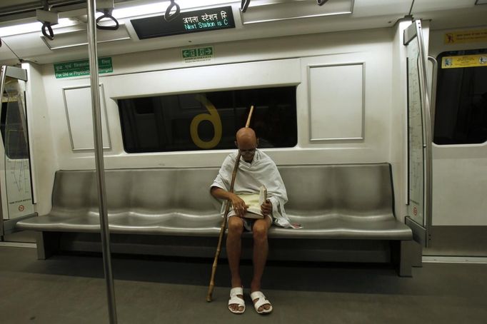 Mahesh Chaturvedi, 63, who dresses up like Mahatma Gandhi, reads a copy of the Bhagavad-Gita, one of Hinduism's most holy books, on a metro train in New Delhi October 2, 2012. Chaturvedi says that the soul of Gandhi resides in him and he has been sent to continue the work of Father of the Nation. After his self proclaimed transformation in 2002 as Gandhi, Chaturvedi has been travelling extensively and plays up to his startling resemblance to Gandhi at protests and demonstrations. Picture taken October 2, 2012. REUTERS/Mansi Thapliyal (INDIA - Tags: SOCIETY TPX IMAGES OF THE DAY) Published: Lis. 26, 2012, 3:57 dop.