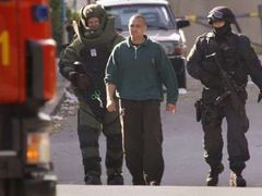 Specialisté švédské policie odvádí muže poté, co jej zbavili pásu s výbušninou.