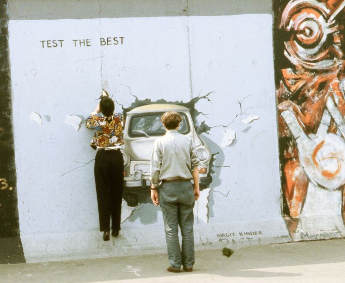 Berlínská zeď, Mühlenstrasse, 1990. Nástěnná malba Birgit Kinder "Test the Best" zobrazuje Trabant prolamující se zdí, symbolizující pád železné opony.