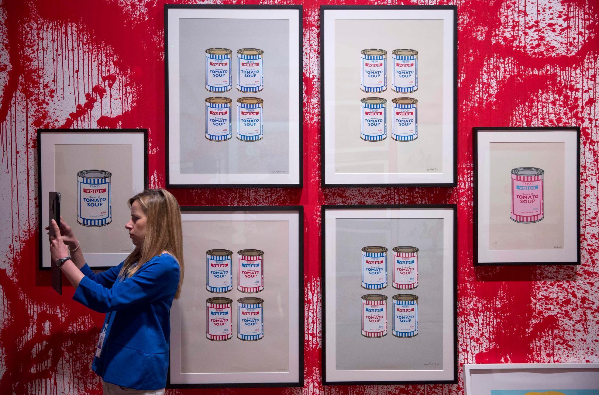 A woman takes a photograph at the Banksy: The Unauthorised Retrospective exhibition at Sotheby's S2 Gallery in London June