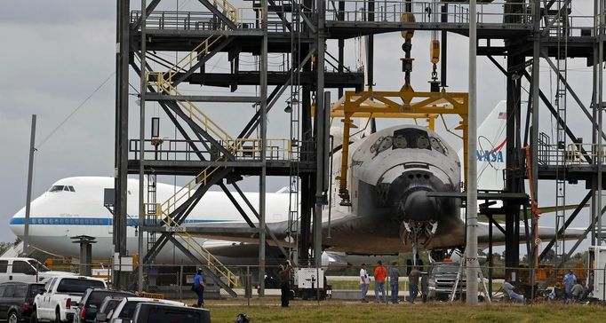 Space center workers walk past the space shuttle Discovery after it was attached to a lifting harness in the Mate Demate facility at Kennedy Space Center in Cape Canaveral