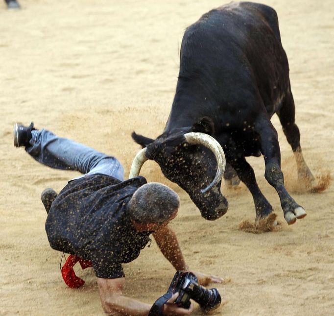 Reuters photographer Joseba Etxaburu is knocked down by a wild cow during festivities in the bullring following the sixth running of the bulls of the San Fermin festival in Pamplona July 12, 2012. Etxaburu suffered some scratches on his right elbow but was able to continue shooting afterwards. REUTERS/Susana Vera (SPAIN - Tags: SOCIETY ANIMALS) Published: Čec. 12, 2012, 9:49 dop.