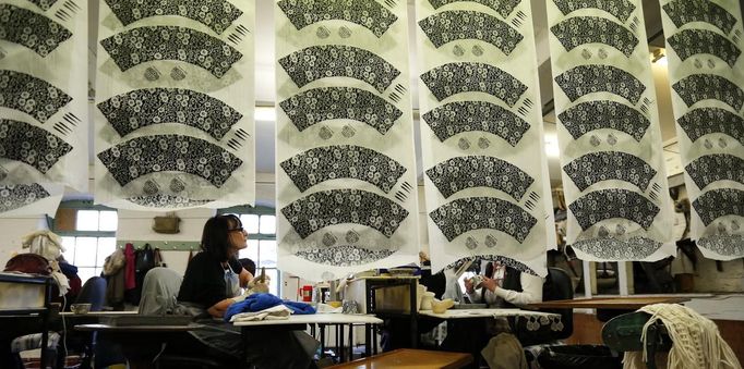 Workers apply tissue paper transfers to cups, as transfers hang to dry in a workshop at the Middleport pottery in Stoke-on-Trent, central England January 22, 2013. The pottery which dates back to 1888 and was rescued from closure in 2009, continues to use traditional methods to produce its range of ceramics and famous Burleigh Ware pottery. REUTERS/Phil Noble (BRITAIN - Tags: BUSINESS EMPLOYMENT SOCIETY) Published: Led. 22, 2013, 5:04 odp.