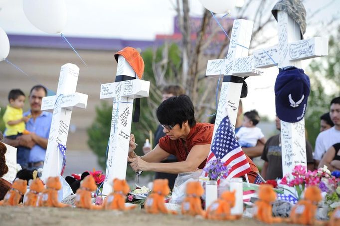 Annette Lucero writes on a cross with a marker at the memorial site for the people killed by a gunman last Friday in the Century 16 movie theater in Aurora, Colorado, July 22, 2012. Residents of a Denver suburb mourned their dead on Sunday from a shooting rampage by a gunman who killed 12 people and wounded 58 after opening fire at a cinema showing the new Batman movie. REUTERS/Jeremy Papasso (UNITED STATES - Tags: CRIME LAW CIVIL UNREST OBITUARY) Published: Čec. 23, 2012, 3:53 dop.