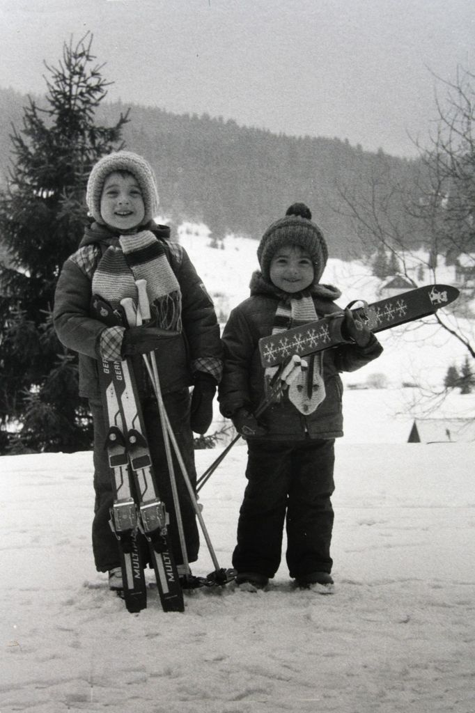 Lyžaři sourozenci poprvé v zimě na horách - Modrava, rok 1984. Syn 4,5 roku má vázání "vyhazovací" a dcera 2,5 roku tzv. "na galoše". Oba čepice, kterým jsme říkali "helm