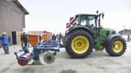 Stroj zapřažený za traktor vytváří v půdě rýhu, do které klade otrávenou návnadu.