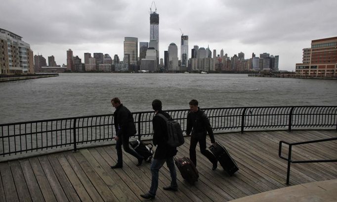 The skyline of New York's Lower Manhattan and One World Trade Center are seen while people pull their luggage at Waterfront in New Jersey, October 28, 2012. Tens of millions of East Coast residents scrambled on Sunday to prepare for Hurricane Sandy, which could make landfall as the largest storm to hit the United States, bringing battering winds, flooding and even heavy snow. REUTERS/Eduardo Munoz (UNITED STATES - Tags: ENVIRONMENT DISASTER)