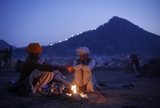 Camel herders warm themselves by a fire at Pushkar Fair in the desert Indian state of Rajasthan November 23, 2012. Many international and domestic tourists throng to Pushkar to witness one of the most colourful and popular fairs in India. Thousands of animals, mainly camels, are brought to the fair to be sold and traded. REUTERS/Danish Siddiqui (INDIA - Tags: SOCIETY ANIMALS) Published: Lis. 23, 2012, 5:23 odp.