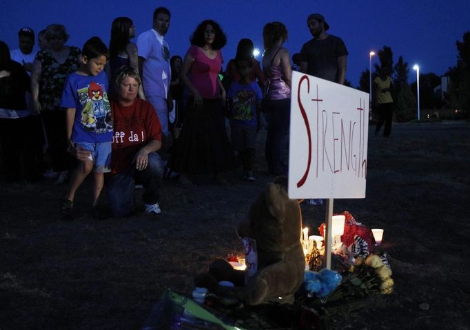 People stand behind a memorial after a vigil for victims behind the theater where a gunman opened fire on moviegoers in Aurora, Colorado July 20, 2012. A total of 71 people were shot in Friday's rampage at the Denver-area movie theater that has left 12 people dead, the local police chief said. The suspect, identified by police as James Eagan Holmes, 24, also booby-trapped his Aurora apartment with sophisticated explosives, creating a hazard for law-enforcement and bomb squad officers who swarmed to the scene. REUTERS/Shannon Stapleton (UNITED STATES - Tags: CRIME LAW) Published: Čec. 21, 2012, 3:06 dop.